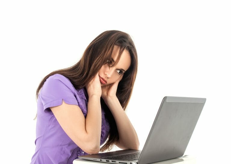 Vrouw met een vermoeide blik zit met haar hand in haar nek achter een laptop