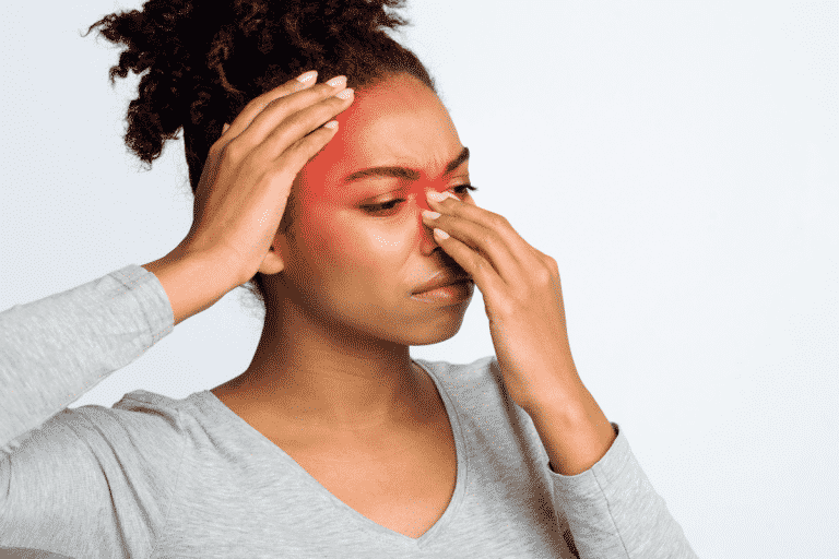Vrouw met haar hand tegen haar voorhoofd en haar neusbrug, waar in rood is aangegeven waar de druk van een bijholteontsteking zit