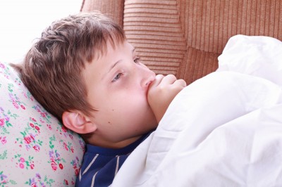Jongen die ziek in bed ligt met een hand bij zijn mond